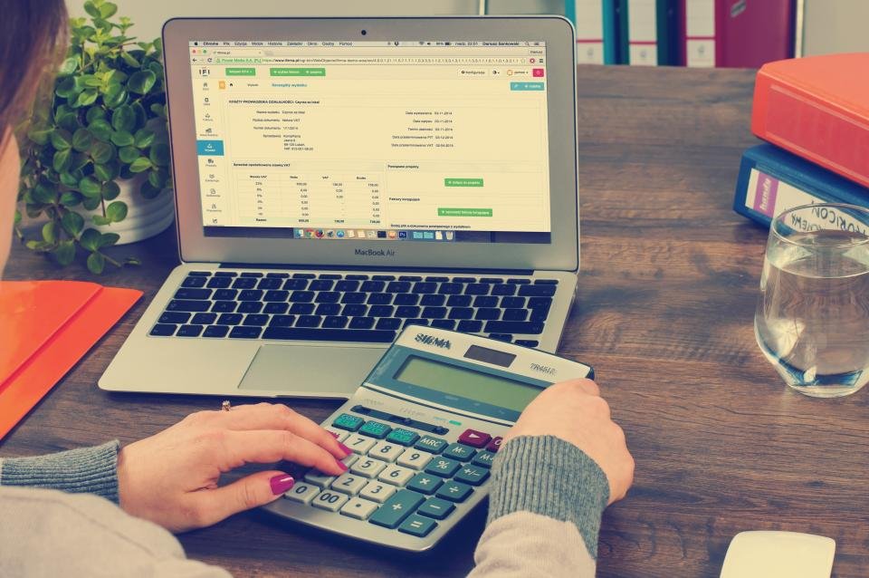 Person using a calculator next to a laptop spreadsheet