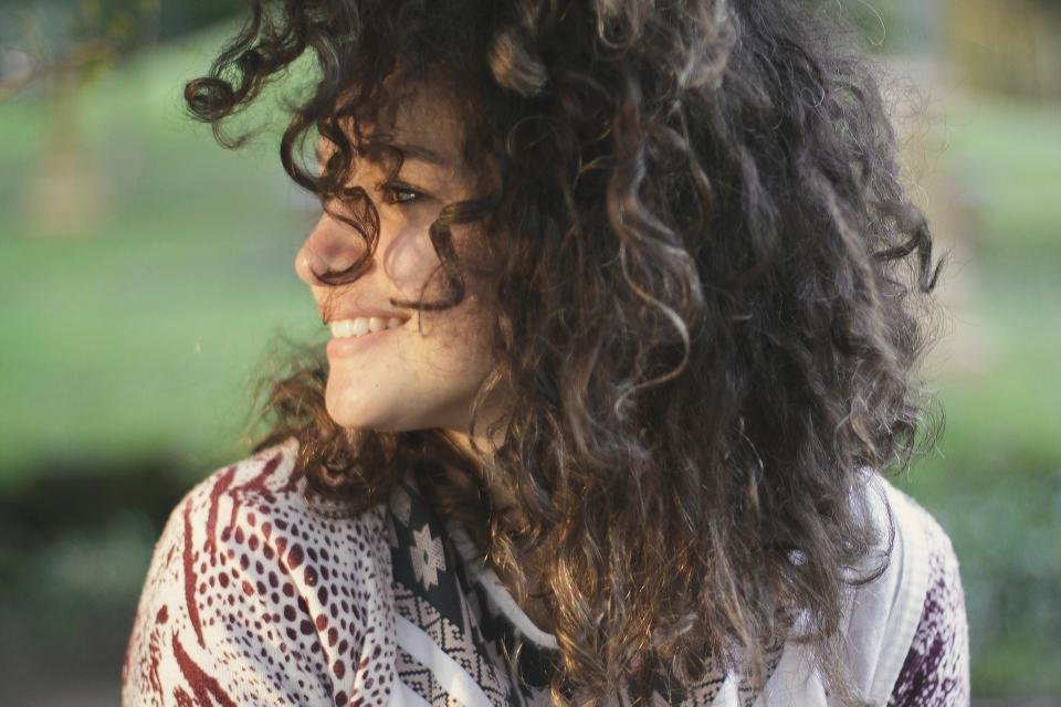 Woman with voluminous curly hair smiling outdoors