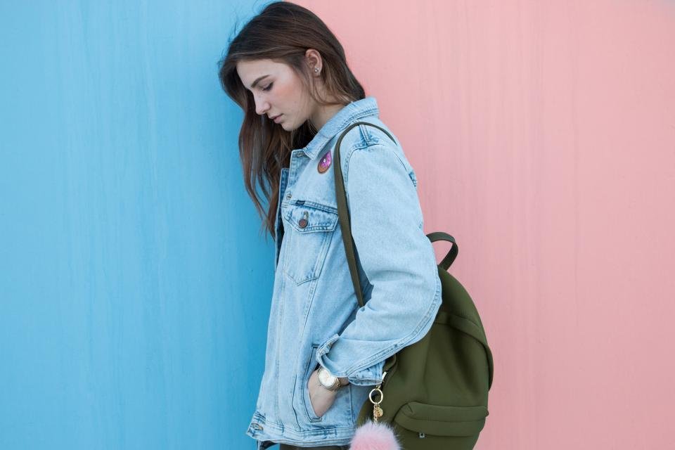 Woman wearing a denim jacket with a backpack against a pastel wall