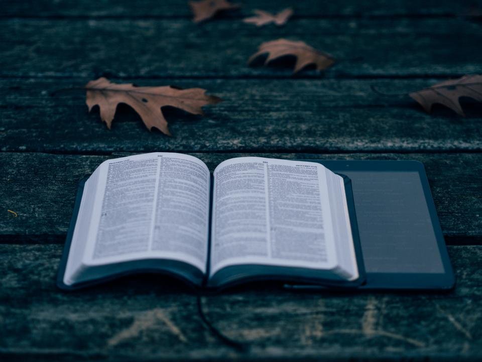 An e-reader beside an open paper book on a wooden table