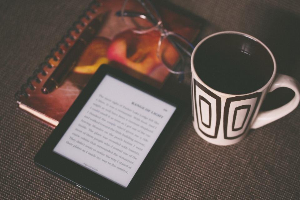 E-reader next to a coffee mug and notebook on a desk