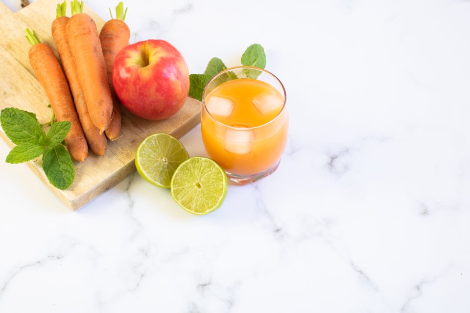 Fresh carrots, apple, limes and a glass of orange juice