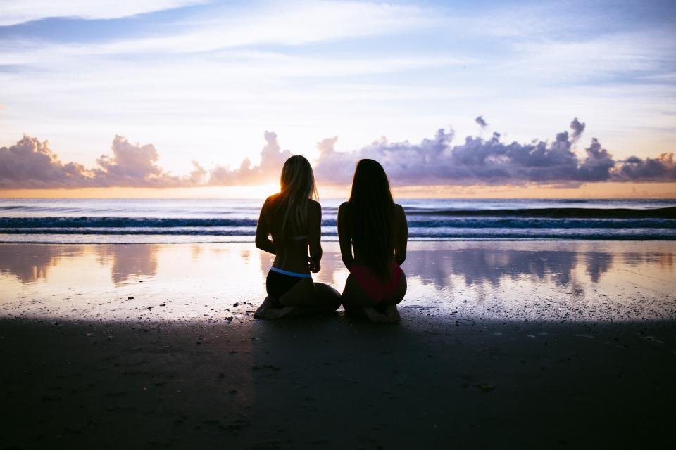 Two friends sitting on the beach at sunset, the kind of memory that inspires gifts for best friend