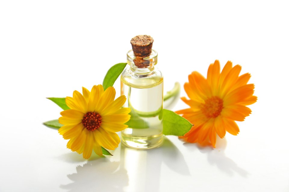 Small glass bottle of oil with orange flowers on a white background