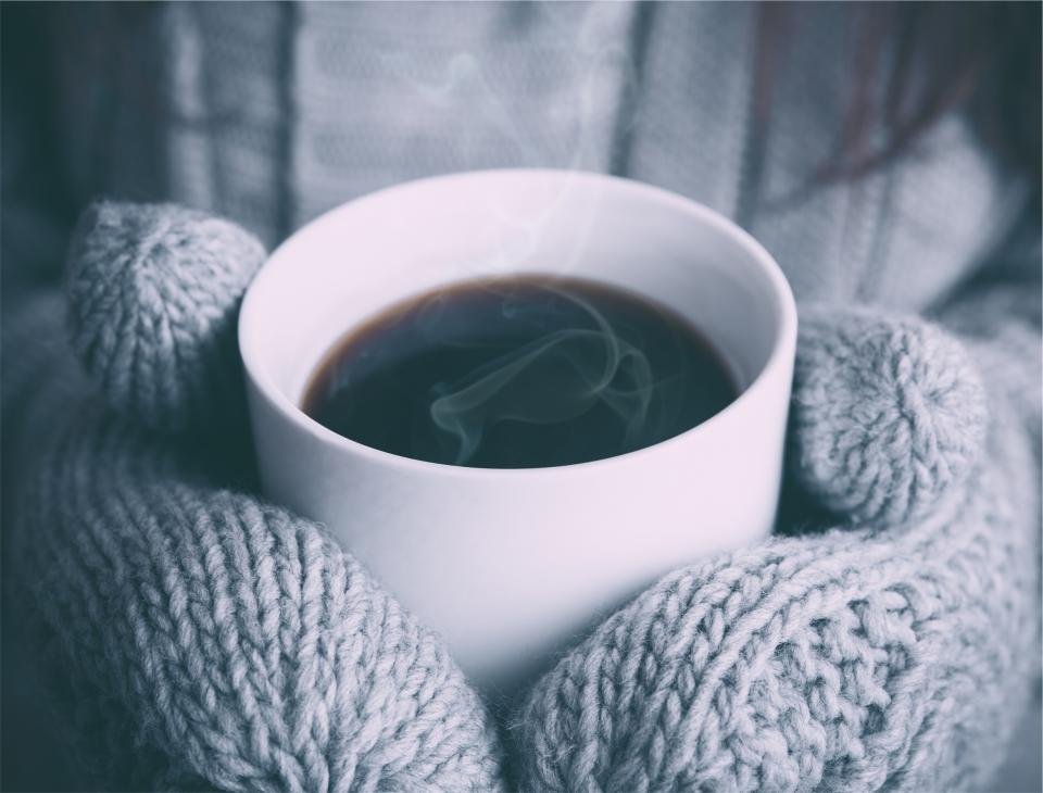 Hands in knitted mittens holding a mug of hot coffee