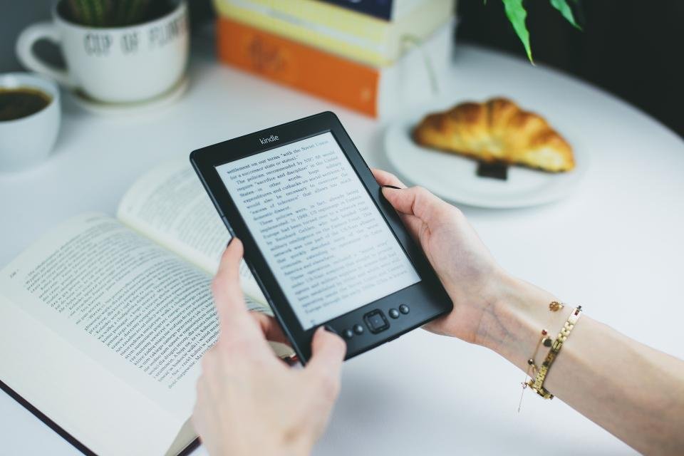 Kindle comparison guide with a woman reading on an e-reader at a cafe table