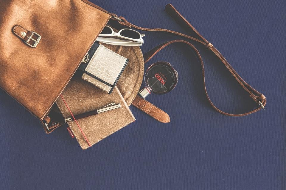 Tan leather handbag with wallet and accessories on a blue background