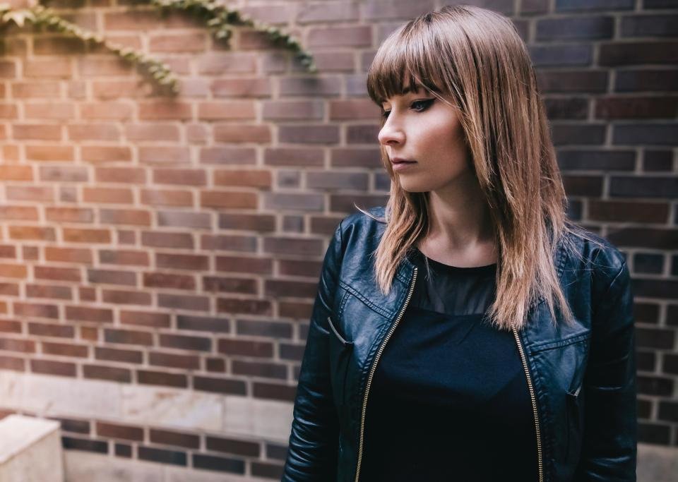 Woman in a black biker jacket by a brick wall, the look faux leather jackets recreate