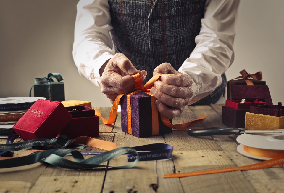 Man wrapping a gift box with ribbon on a wooden table