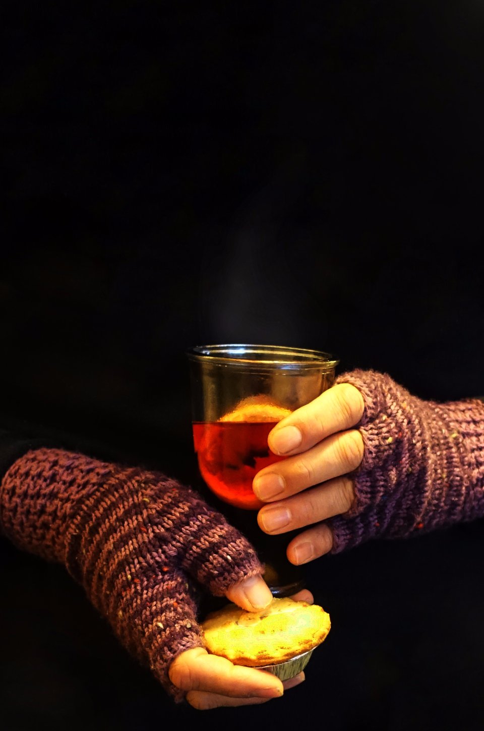 Gloved hand holding a glass of mulled wine on a winter evening