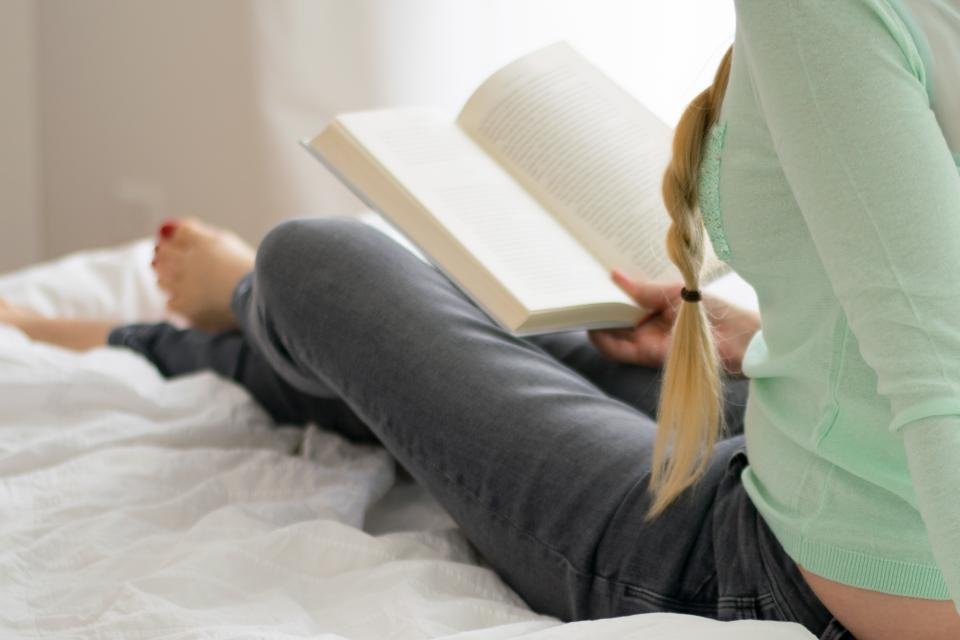 Woman reading a book propped up on bed pillows
