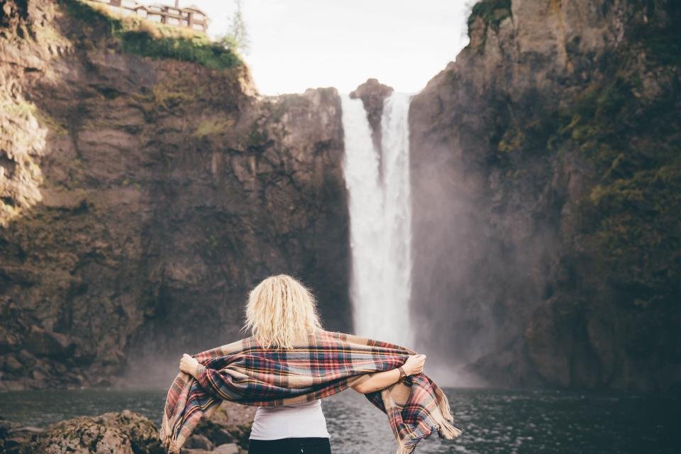 Woman holding a plaid scarf in front of a waterfall