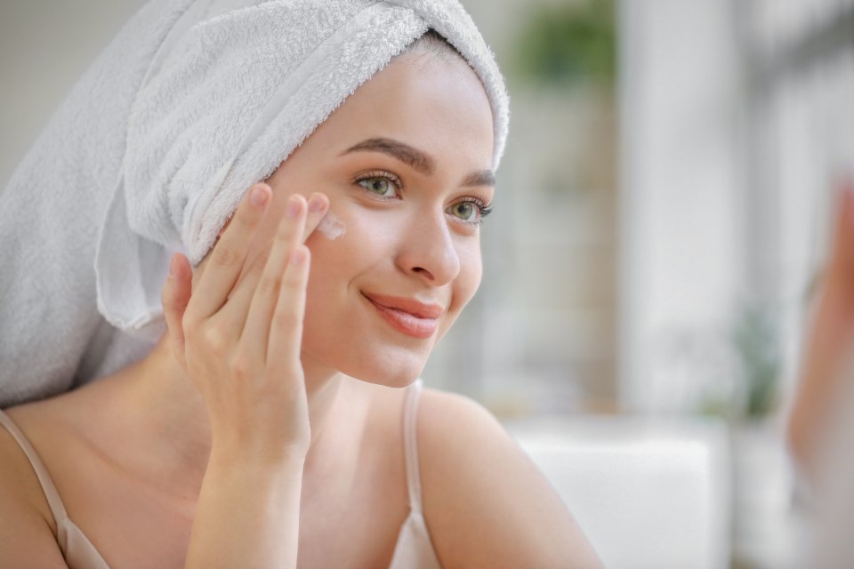 Woman with a towel in her hair applying cream during a skincare routine