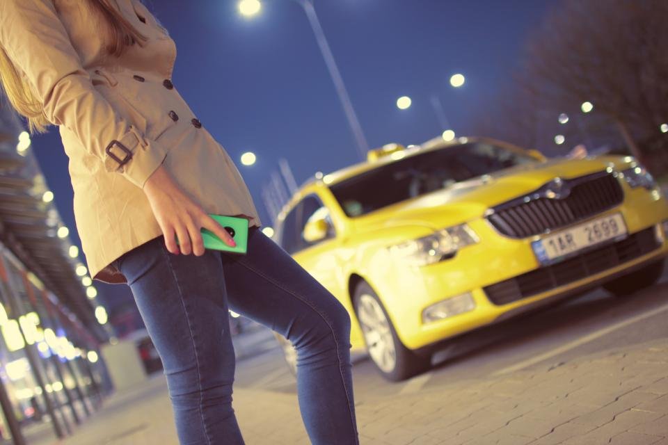 Woman in a belted trench coat hailing a taxi at night