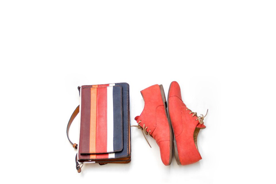 Striped wallet next to red lace up shoes on a white background