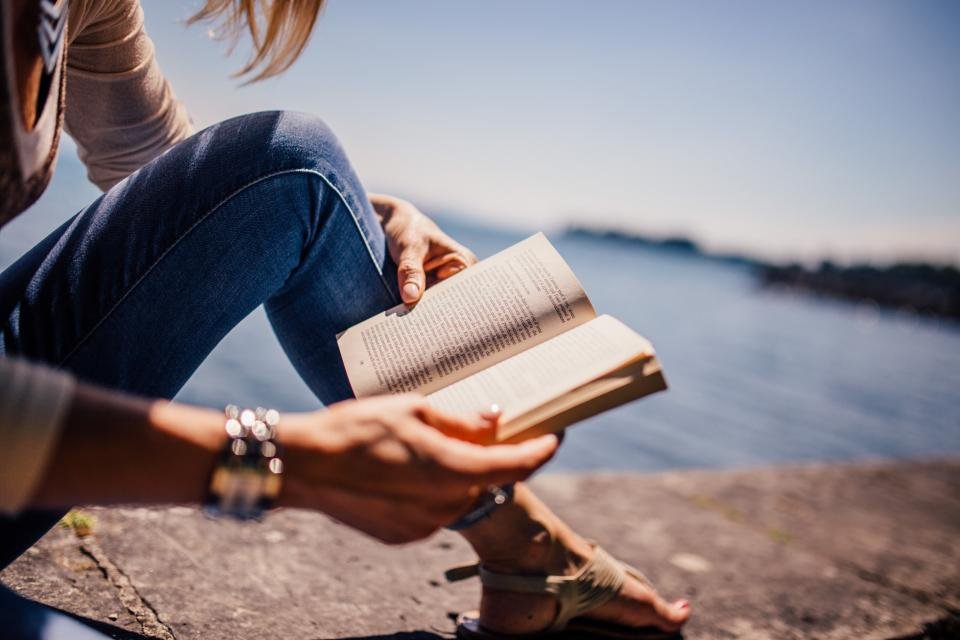 Woman reading outdoors by the water, one of the best self help books for women in hand