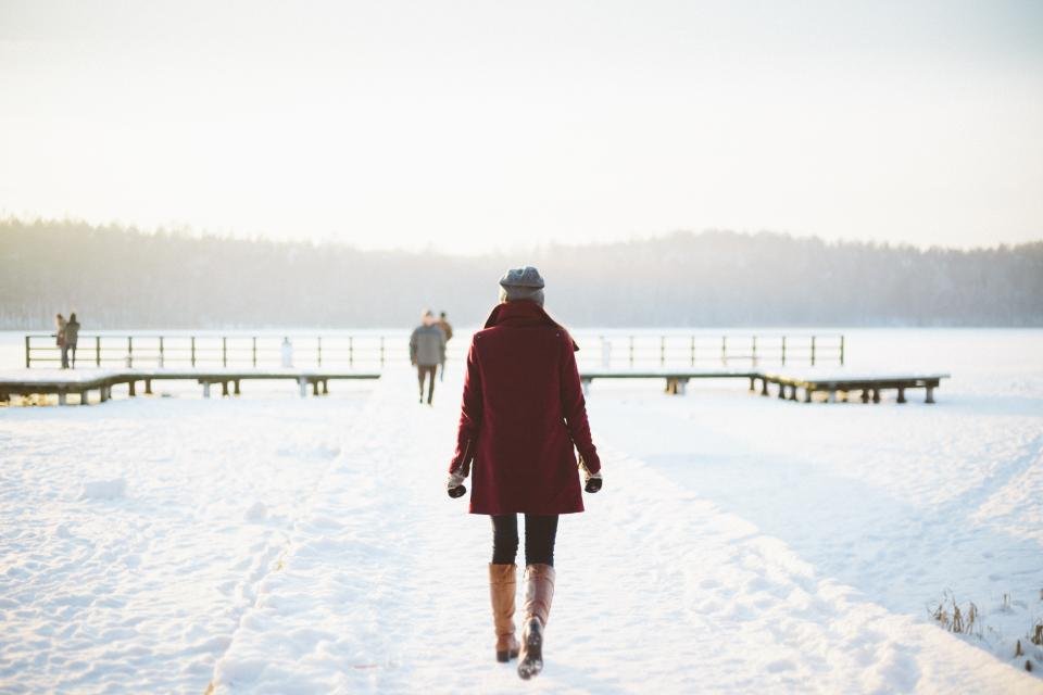 Woman in a red coat walking in snow in tights and boots