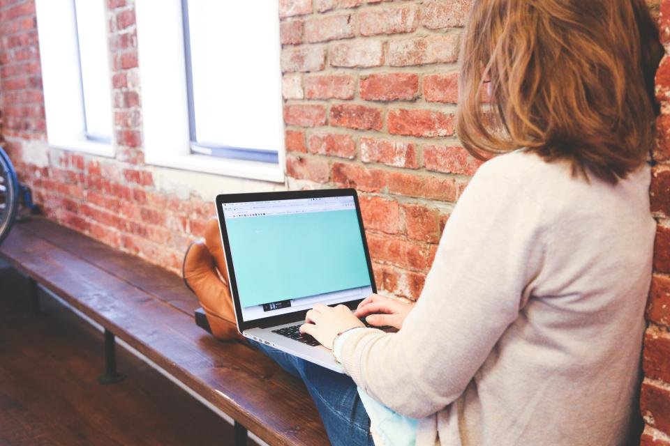 Woman typing on a laptop by a brick wall, ready to pack it into a laptop bag