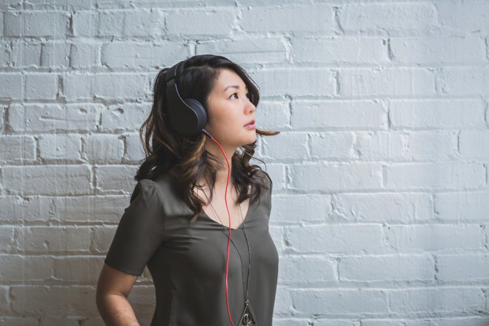 Woman listening with the best noise cancelling headphones against a white brick wall